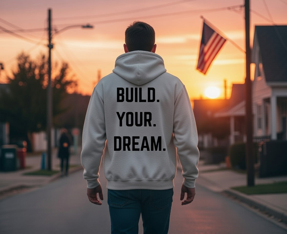 Person wearing a hoodie with 'BUILD. YOUR. DREAM.' text at sunset.