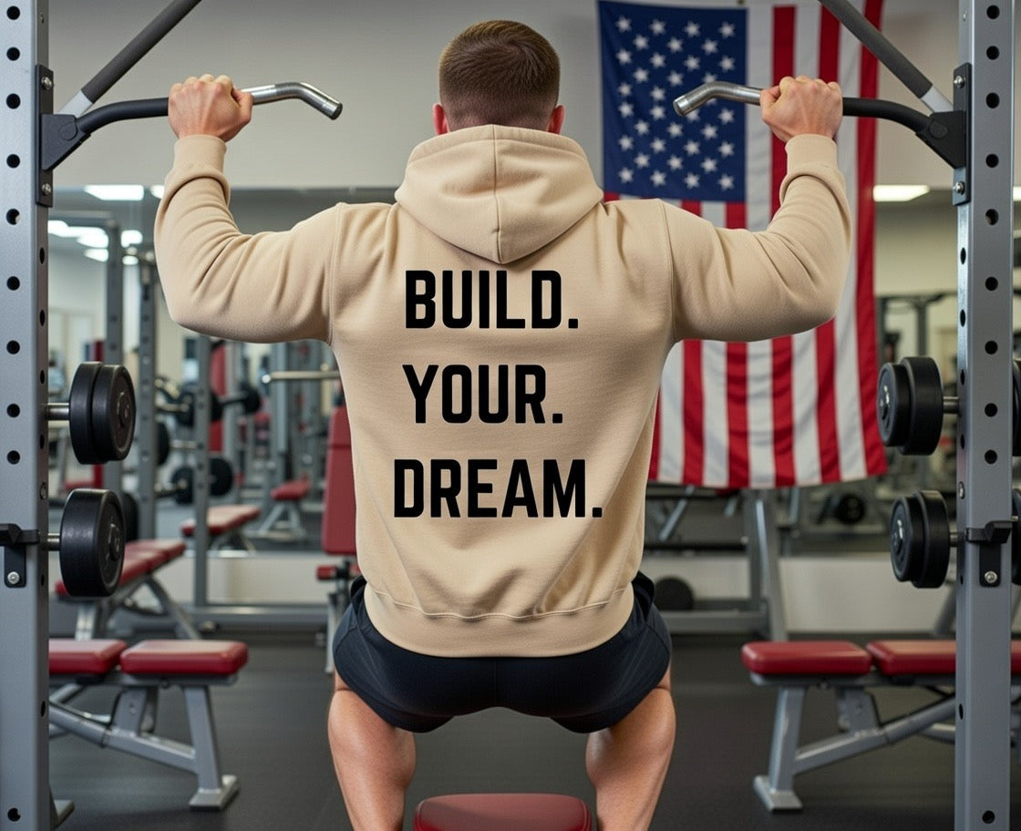Person in a gym wearing a hoodie with 'Build Your Dream' text, American flag in the background